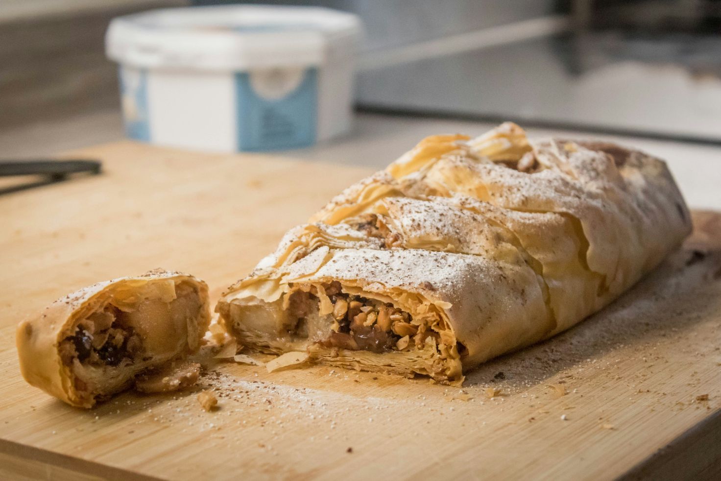 Nahaufnahme eines angeschnittenen Apfelstrudels auf einem Holzbrett, bestäubt mit Puderzucker.