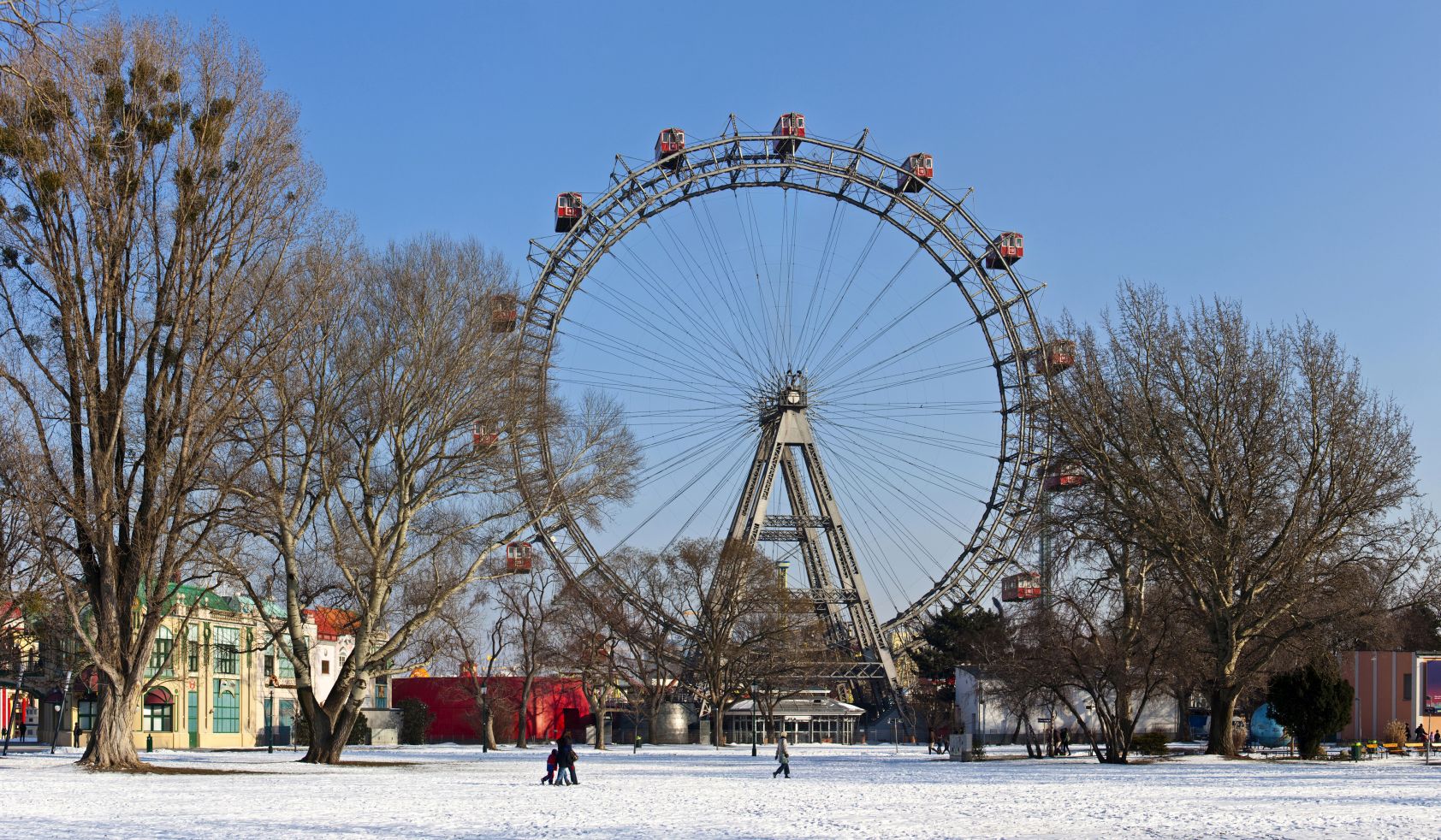 Das Wiener Riesenrad im Prater bei winterlichem Wetter, mit schneebedecktem Boden und kahlen Bäumen im Vordergrund.