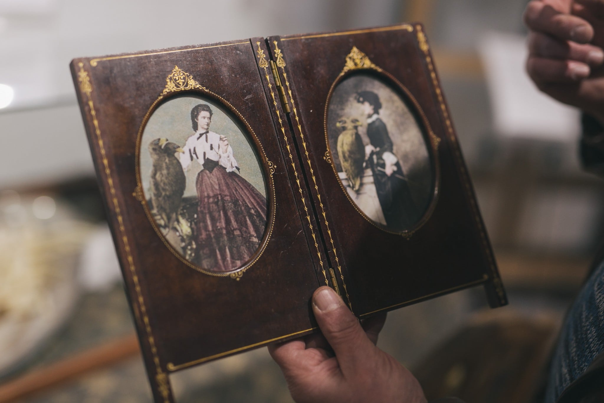 Eine Person hält ein altes Fotoalbum mit zwei Portraits von Kaiserin Sisi in traditioneller Kleidung.