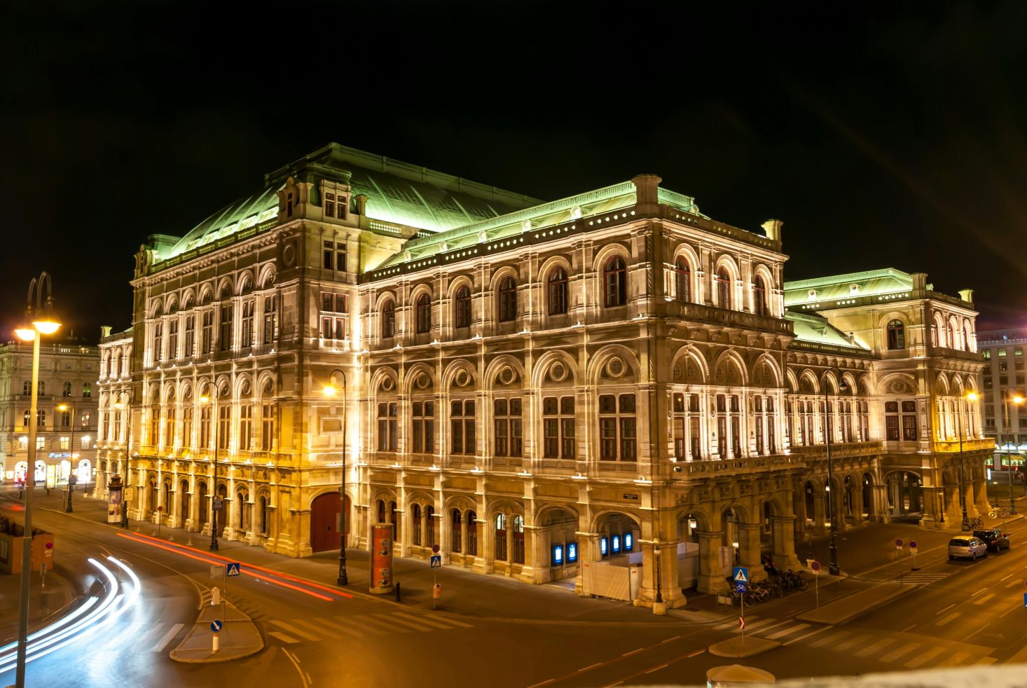 Beleuchtete Wiener Staatsoper bei Nacht mit Straßenverkehr und Lichtspuren im Vordergrund