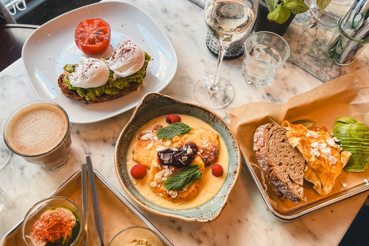  Tisch mit einem Frühstück bestehend aus Avocado-Toast, Pancakes, Brot, Aufstrichen und Getränken in einem Wiener Café.